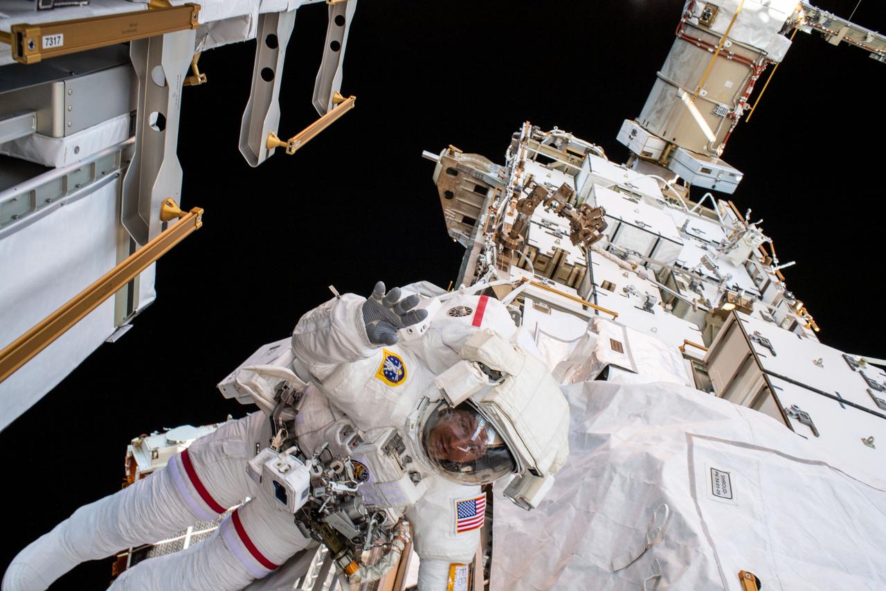 iss061e005520 (Oct. 11, 2019) --- NASA astronaut Andrew Morgan waves to the camera while tethered on the Port 6 (P6) truss segment of the International Space Stations. He and fellow NASA astronaut Christina Koch (out of frame) worked to replace older hydrogen-nickel batteries with newer, more powerful lithium-ion batteries on the P6 truss during the six-hour and 45-minute spacewalk.