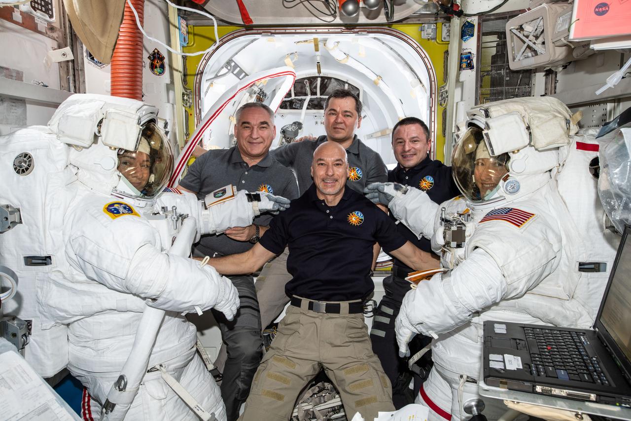 The International Space Station Expedition 61 crew pauses for a photo as NASA Astronauts Jessica Meir and Christina Koch prepare to exit the space station to begin the first all-female spacewalk in history on Oct. 18, 2019. The astronauts replaced a faulty battery charge/discharge unit (BCDU) that failed to activate following the Oct. 11 installation of new lithium-ion batteries on the space station’s exterior structure. The BCDUs regulate the amount of charge put into the batteries that collect energy from the station’s solar arrays to power station systems during periods when the station orbits during nighttime passes around Earth. Though the BCDU failure has not impacted station operations or crew safety, it does prevent the new batteries from providing increased station power.