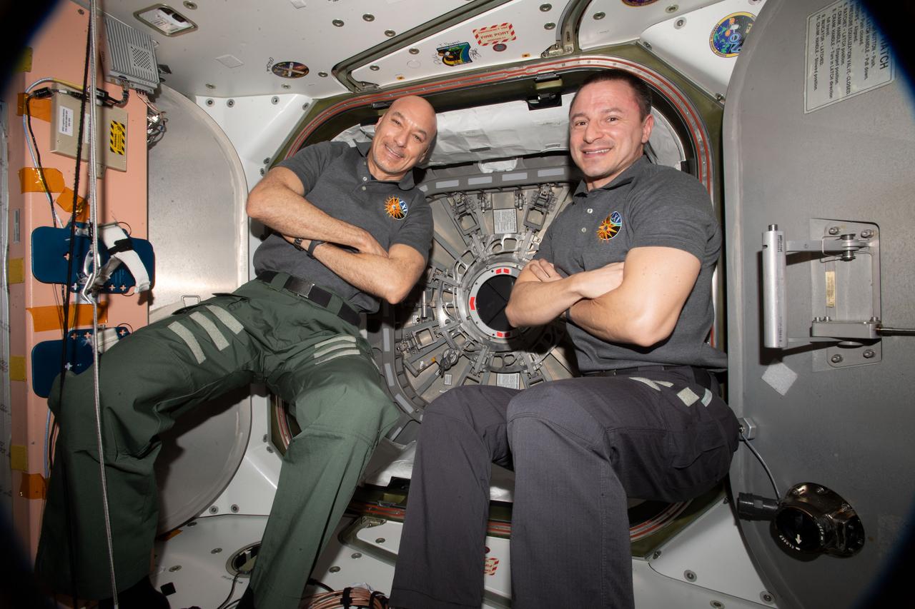 iss061e028299 (Nov. 4, 2019) --- Astronauts (from left) Luca Parmitano of ESA (European Space Agency) and Andrew Morgan of NASA pose for a portrait in front the hatch that opens to the Cygnus space freighter from Northrop Grumman.