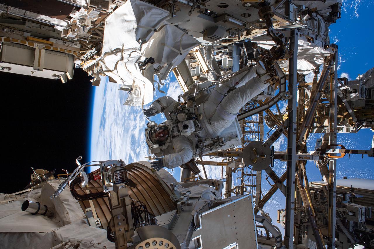 iss061e040844 (Nov. 15, 2019) --- NASA astronaut Andrew Morgan waves as he is photographed seemingly camouflaged among the Alpha Magnetic Spectrometer (lower left) and other International Space Station hardware during the first spacewalk to repair the cosmic particle detector.
