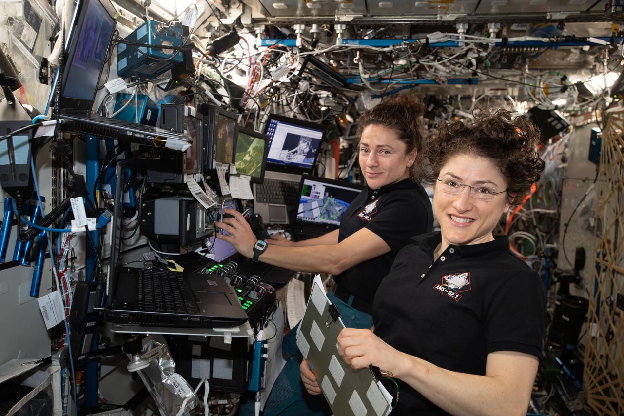 iss061e045472 (Nov. 15, 2019) --- NASA astronauts (from left ) Jessica Meir and Christina Koch are at the robotics workstation controlling the Canadarm2 robotic arm to support the first spacewalk to repair the Alpha Magnetic Spectrometer (AMS), the International Space Station's cosmic particle detector. Astronauts Luca Parmitano of ESA (European Space Agency) and Andrew Morgan of NASA worked six hours and 39 minutes in the vacuum of space during the first of at least four planned AMS repair spacewalks.