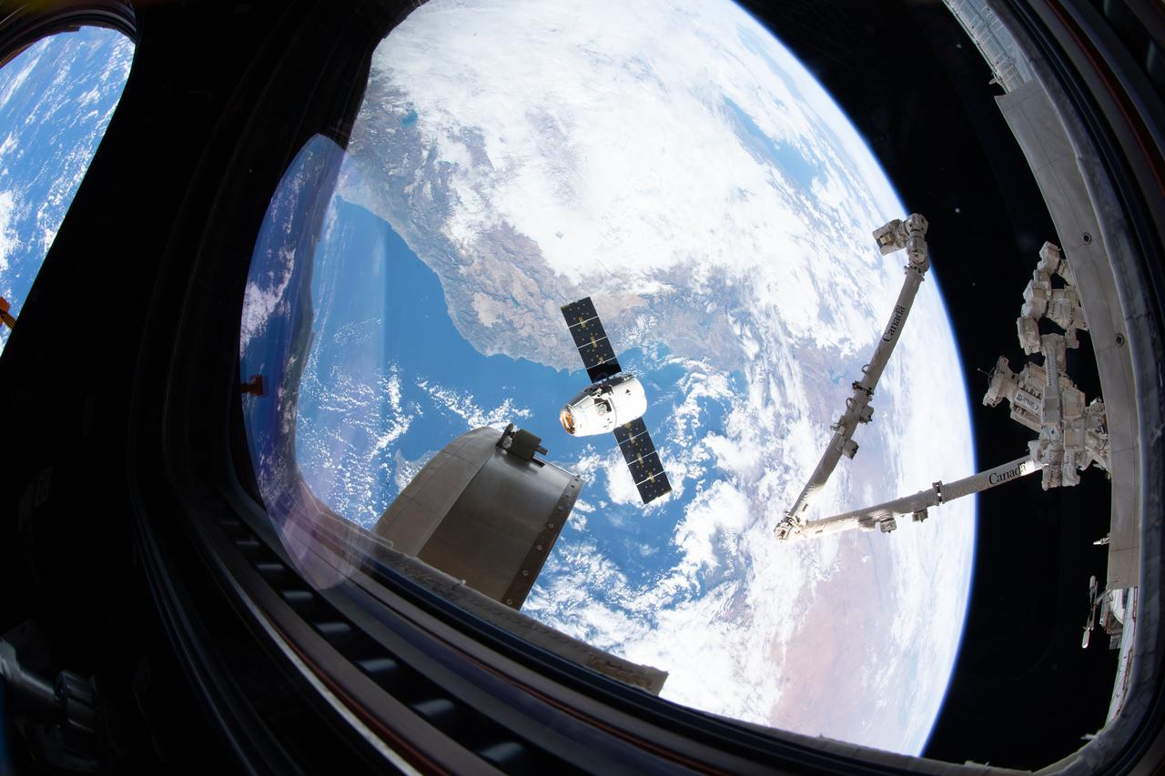 iss061e070168 (Dec. 8, 2019) --- This view from the cupola, the International Space Station's "window to the world," shows the SpaceX Dragon resupply ship slowly approaching the orbiting lab as both spacecraft were orbiting 258 miles above the Mediterranean Sea. The Canadarm2 robotic arm (at right) is poised to reach out and grapple Dragon and install the U.S. space freighter to the Harmony module.