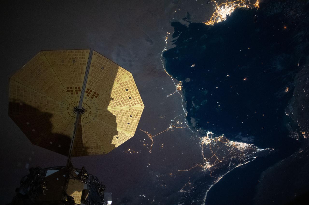 iss063e006718 (May 5, 2020) --- This nighttime image from the International Space Station shows the Persian Gulf city of Doha, Qatar (top right) and the United Arab Emirates cities (bottom right) of Abu Dhabi, Dubai and Ali Ain. In the foreground, is one of the cymbal-shaped UltraFLex solar arrays that powers the Cygnus space freighter from Northrop Grumman.