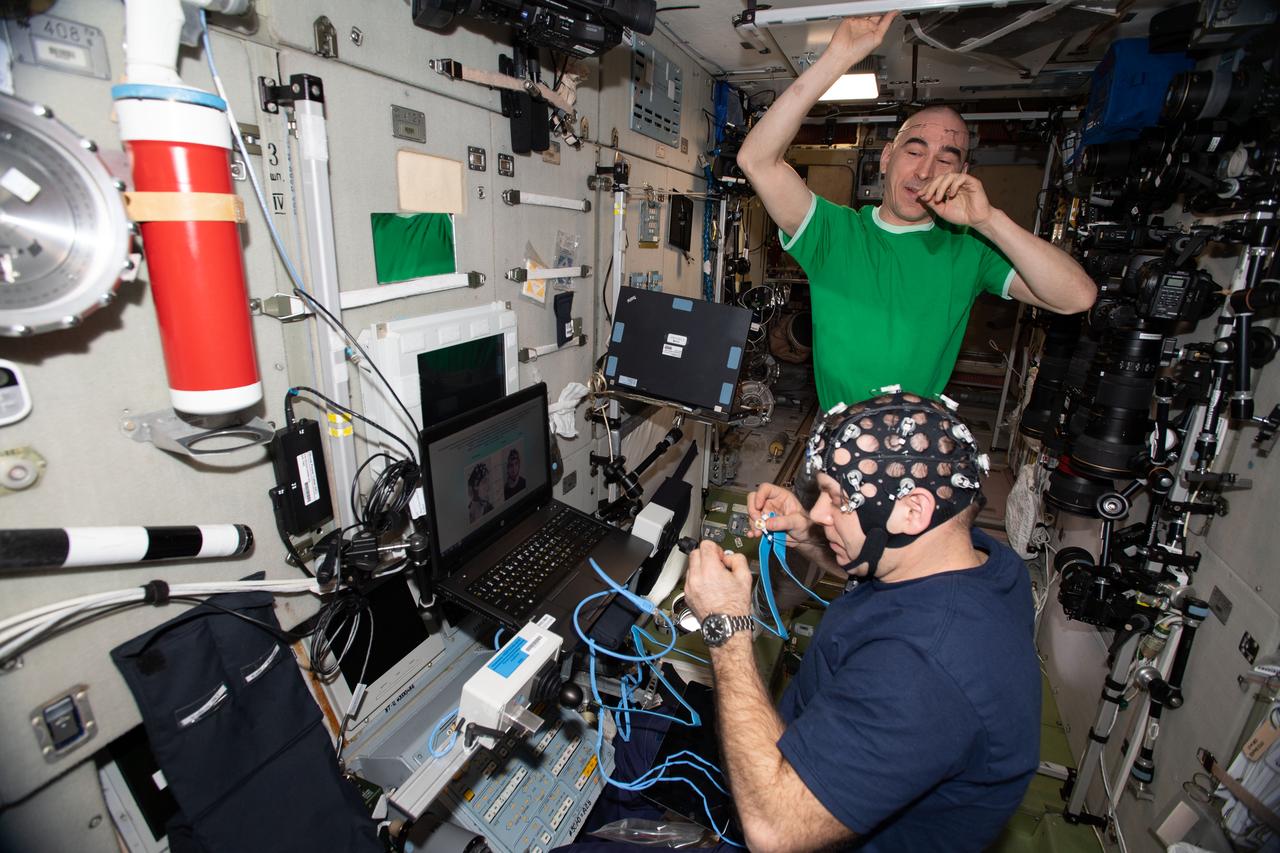 iss063e013834 (May 20, 2020) --- Roscosmos cosmonauts and Expedition 63 Flight Engineers Ivan Vagner (foreground) and Anatoly Ivanishin are pictured inside the International Space Station's Zvezda service module. Vagner is wearing Neurolab hardware for the Russian Pilot-T experiment that explores how space travelers may pilot future spacecraft on planetary missions.