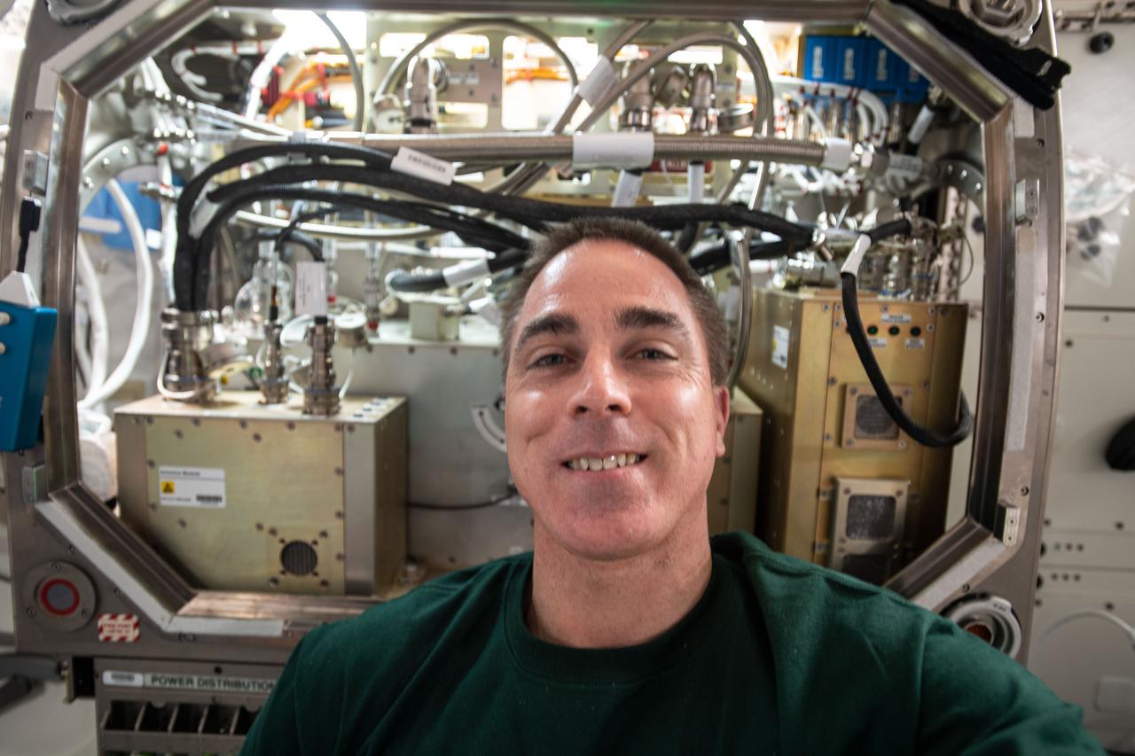 iss063e068516 (Aug. 12, 2020) --- NASA astronaut and Expedition 63 Commander Chris Cassidy poses for a portrait in front of the Microgravity Science Glovebox as he was setting up the Packed Bed Reactor Experiment inside the research device. The new science hardware is exploring technology to support water recovery, planetary surface processing and oxygen production.
