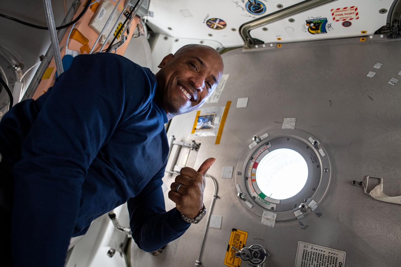 iss064e020173 (Jan. 6, 2021) --- NASA astronaut Victor Glover gives a "thumbs up" in front of the International Space Station's Unity module hatch window. Robotics controllers commanded the Canadarm2 robotic arm to uninstall the Northrop Grumman Cygnus space freighter from Unity's Earth-facing port a few hours earlier before releasing it after 93 days attached to the station.