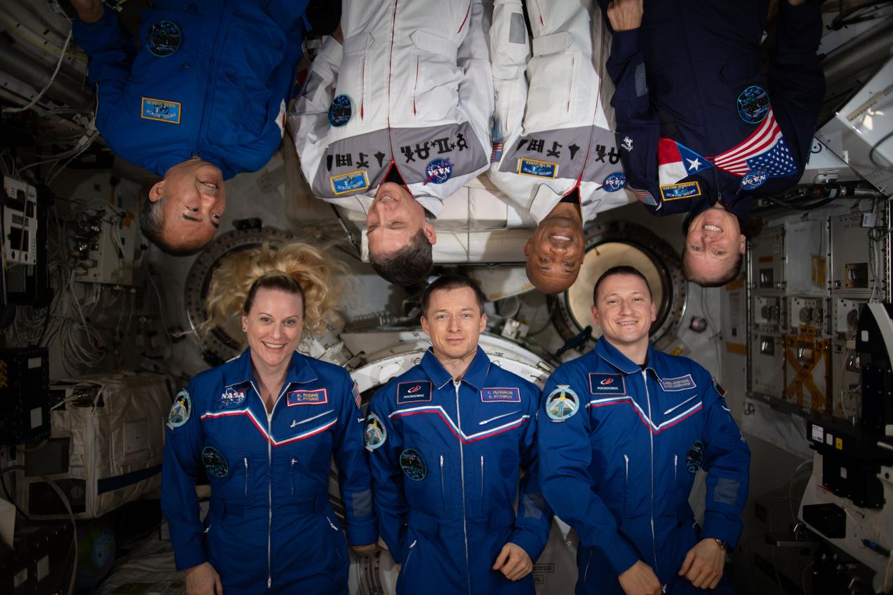 iss064e020868 (Jan. 6, 2021) --- The seven-member Expedition 64 crew poses for a portrait inside the International Space Station's Kibo laboratory module from JAXA (Japan Aerospace Exploration Module). In the bottom row from left are, NASA astronaut Kate Rubins and Roscosmos cosmonauts Sergey Ryzhikov and Sergey Kud-Sverchkov. In the top row are, JAXA astronaut Soichi Noguchi and NASA astronauts Michael Hopkins, Victor Glover and Shannon Walker.  Glover and Hopkins are wearing white uniforms that commemorate the NASA human spaceflight programs Mercury, Gemini, Apollo, Apollo-Soyuz, Space Shuttle, Shuttle-Mir, International Space Station and Commercial Crew.