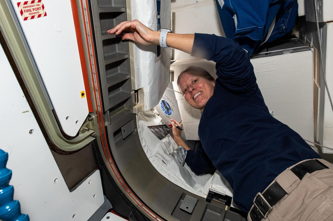 iss064e031802 (Feb. 11,2021) --- NASA astronaut and Expedition 64 Flight Engineer Shannon Walker signs her name near her mission's insignia sticker in the vestibule between the Tranquility module and the NanoRacks Bishop airlock.