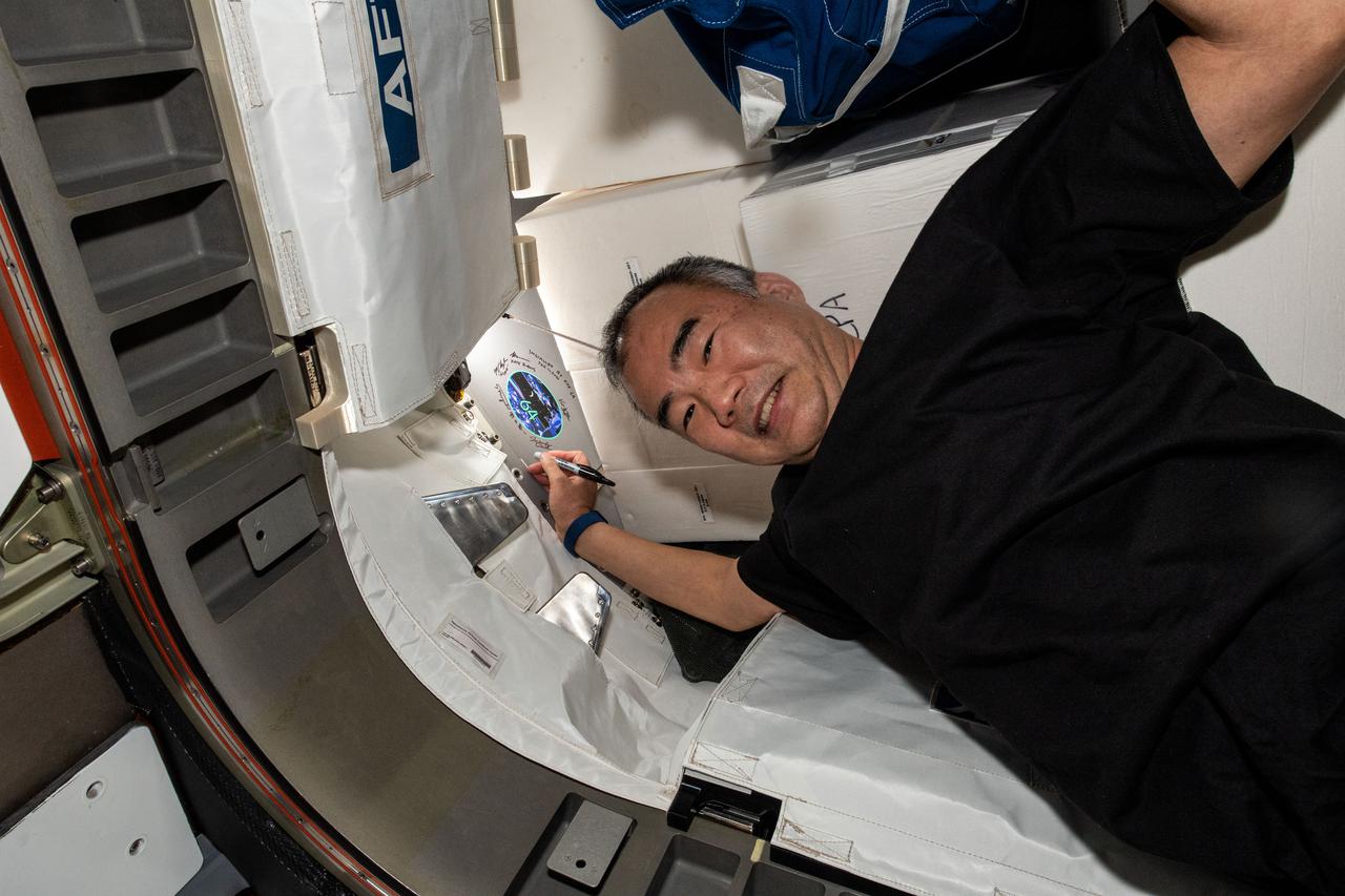 iss064e031806 (Feb. 11,2021) --- JAXA (Japan Aerospace Exploration Agency) astronaut and Expedition 64 Flight Engineer Soichi Noguchi signs his name near his mission's insignia sticker in the vestibule between the Tranquility module and the NanoRacks Bishop airlock.