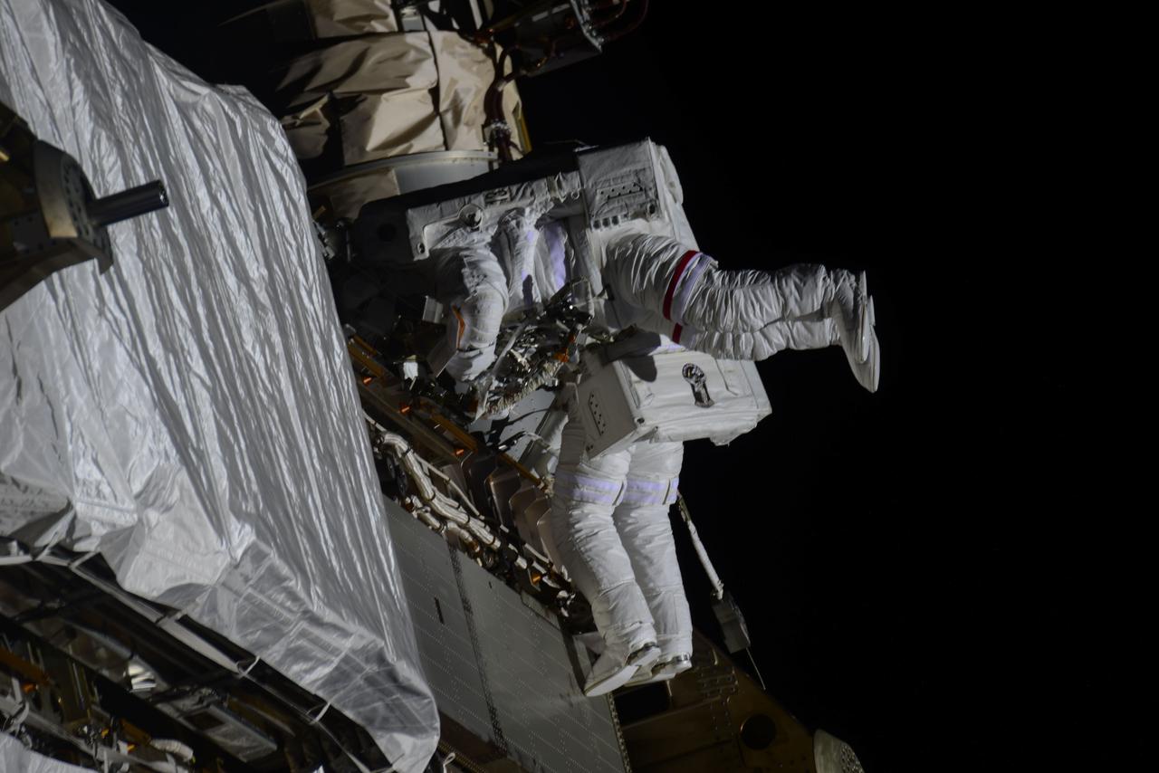 iss064e039327 (Feb. 28, 2021) --- NASA astronauts Kate Rubins (foreground) and Victor Glover are pictured during a spacewalk to install solar array modification kits on the International Space Station. The maintenance work will support new, more powerful solar arrays that will be delivered on upcoming SpaceX Dragon cargo missions. Credit: Roscosmos