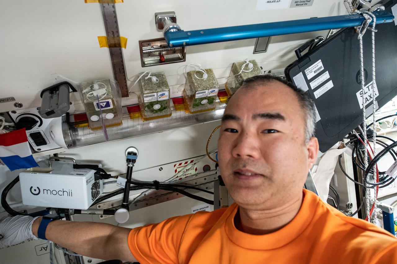iss064e040580 (March 9, 2021) --- JAXA (Japan Aerospace Exploration Agency) astronaut Soichi Noguchi poses with plants growing inside containers for the Asian Herbs study. The space botany investigation is exploring ways to cultivate fast-growing plants used for traditional medicine and food flavoring.