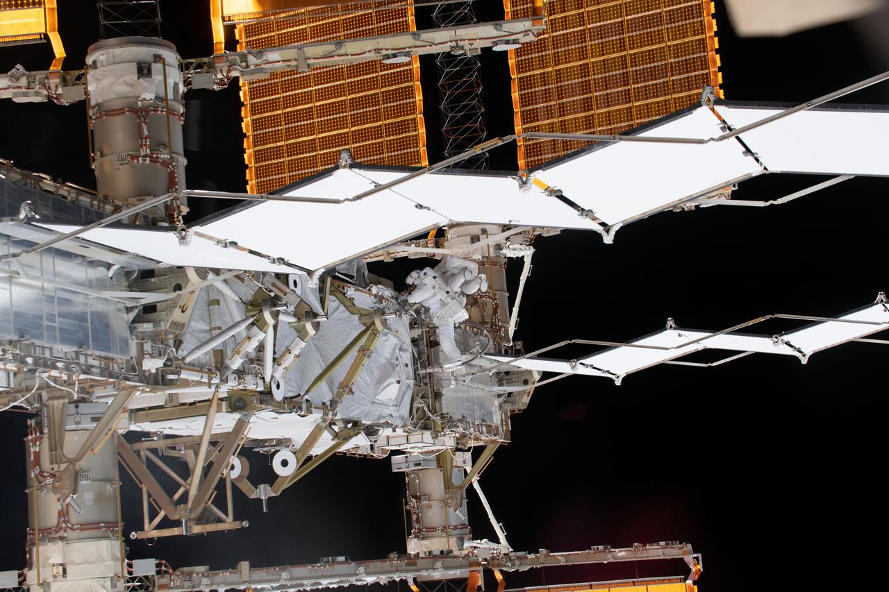 iss064e041634 (March 13, 2021) --- NASA spacewalkers Michael Hopkins and Victor Glover (both at center) are dwarfed by the International Space Station's main solar arrays and radiators during a spacewalk to service the station’s cooling system and communications gear.