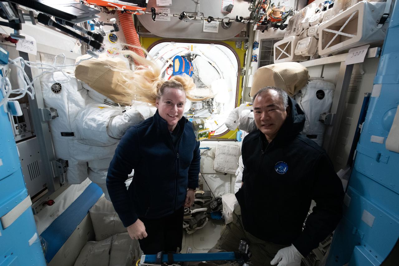 iss064e044335 (March 18, 2021) --- Astronauts Kate Rubins of NASA and Soichi Noguchi of JAXA (Japan Aerospace Exploration Agency) are pictured in front of a pair U.S. spacesuits inside the International Space Station's Quest airlock.