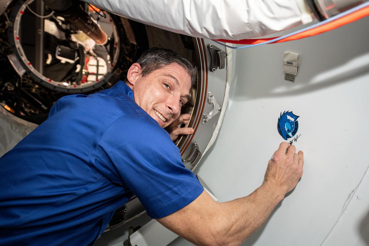 iss064e052199 (April 4, 2021) --- SpaceX Crew-1 Commander Michael Hopkins of NASA signs his name next to the mission insignia affixed to the vestibule between the Crew Dragon spacecraft and the Harmony module's forward international docking adapter.