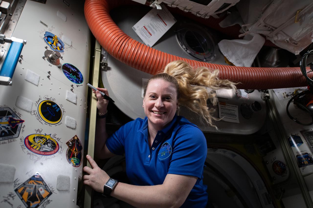 iss064e053364 (April 7, 2021) --- NASA astronaut and Expedition 64 Flight Engineer Kate Rubins signs her name next to the Expedition 64 mission insignia affixed inside the International Space Station.