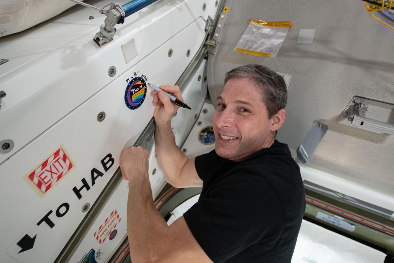 iss064e053415 (April 6, 2021) --- NASA astronaut and Expedition 64 Flight Engineer Michael Hopkins applies his signature to the Unity module's vestibule that leads to the Cygnus space freighter from Northrop Grumman.