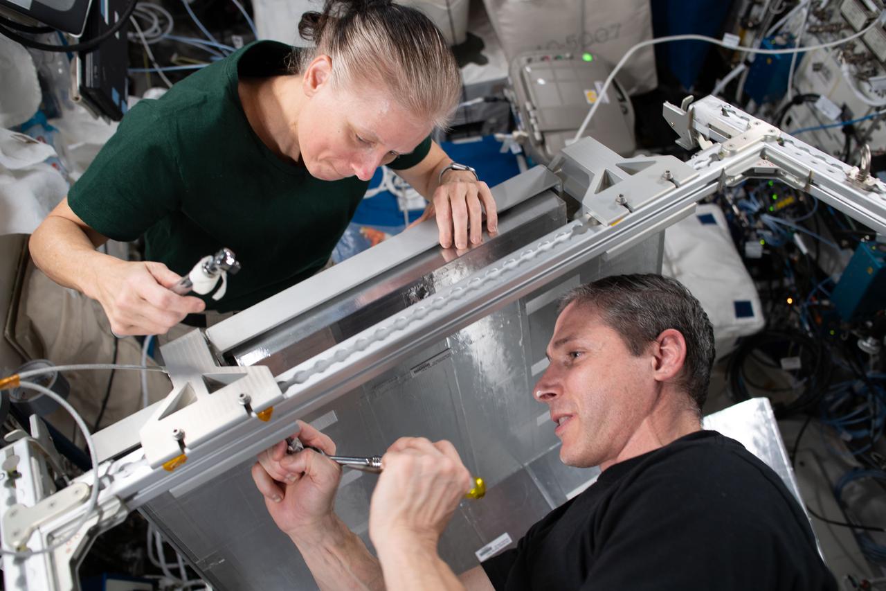 iss064e053521 (April 7, 2021) --- NASA Flight Engineers Shannon Walker and Michael Hopkins install temporary sleeping quarters inside the Columbus laboratory module from the European Space Agency. The new Crew Alternate Sleep Accommodation, which can also be converted to a cargo storage rack, will allow extra space for the short period when up to 11 crew members will be occupying the International Space Station in April.