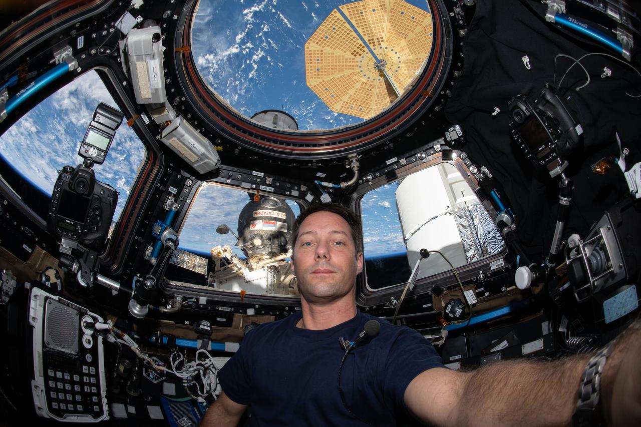 iss065e034024 (May 12, 2021) --- Expedition 65 Flight Engineer Thomas Pesquet of ESA (European Space Agency) is pictured inside the International Space Station's "window to the world," the cupola. Just outside the cupola are two spacecraft. At right, is the U.S. Northrop Grumman Cygnus space freighter with one of its two prominent cymbal-shaped UtraFlex solar arrays. To the left, and directly behind Pesquet, is the Soyuz MS-17 crew ship.