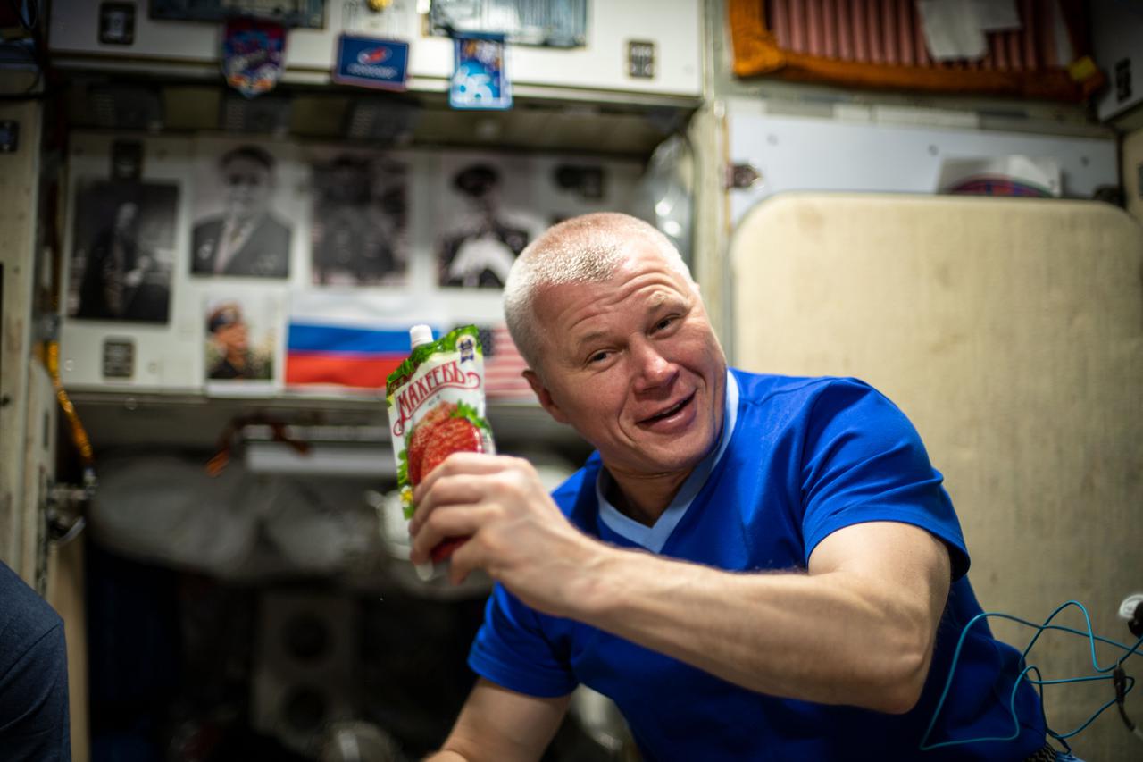 iss065e099693 (June 11, 2021) --- Roscosmos cosmonaut and Expedition 65 Flight Engineer Oleg Novitskiy shows off a drink bag during a midday meal aboard the International Space Station.
