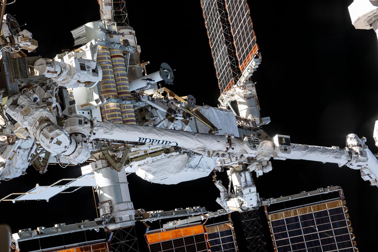 iss065e144314 (June 16, 2021) --- Spacewalkers (near bottom center) Thomas Pesquet and Shane Kimbrough are dwarfed by the Canadarm2 robotic arm as they work to install a new roll out solar array on the International Space Station's Port-6 truss structure.