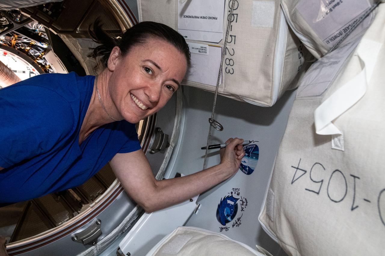 iss065e162499 (July 6, 2021) --- NASA astronaut and Expedition 65 Flight Engineer Megan McArthur signs her name next to the SpaceX CRS-22 cargo mission sticker attached to the vestibule between the SpaceX Cargo Dragon resupply ship and the Harmony module's space-facing international docking adapter.