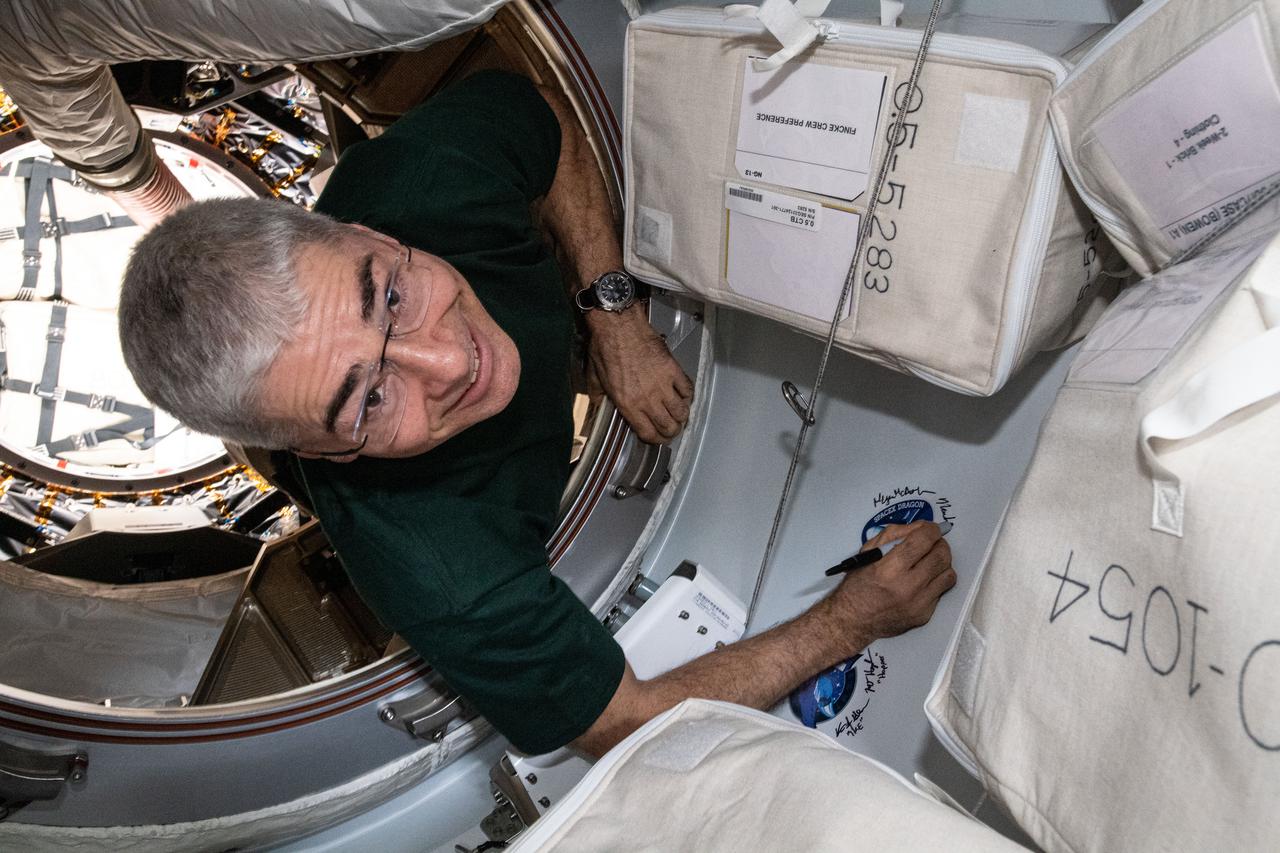 iss065e162500 (July 6, 2021) --- NASA astronaut and Expedition 65 Flight Engineer Mark Vande Hei signs his name next to the SpaceX CRS-22 cargo mission sticker attached to the vestibule between the SpaceX Cargo Dragon resupply ship and the Harmony module's space-facing international docking adapter.