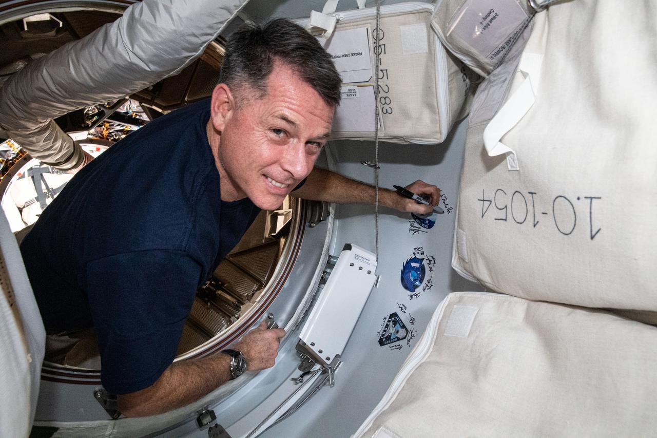 iss065e162506 (July 6, 2021) --- NASA astronaut and Expedition 65 Flight Engineer Shane Kimbrough signs his name next to the SpaceX CRS-22 cargo mission sticker attached to the vestibule between the SpaceX Cargo Dragon resupply ship and the Harmony module's space-facing international docking adapter.