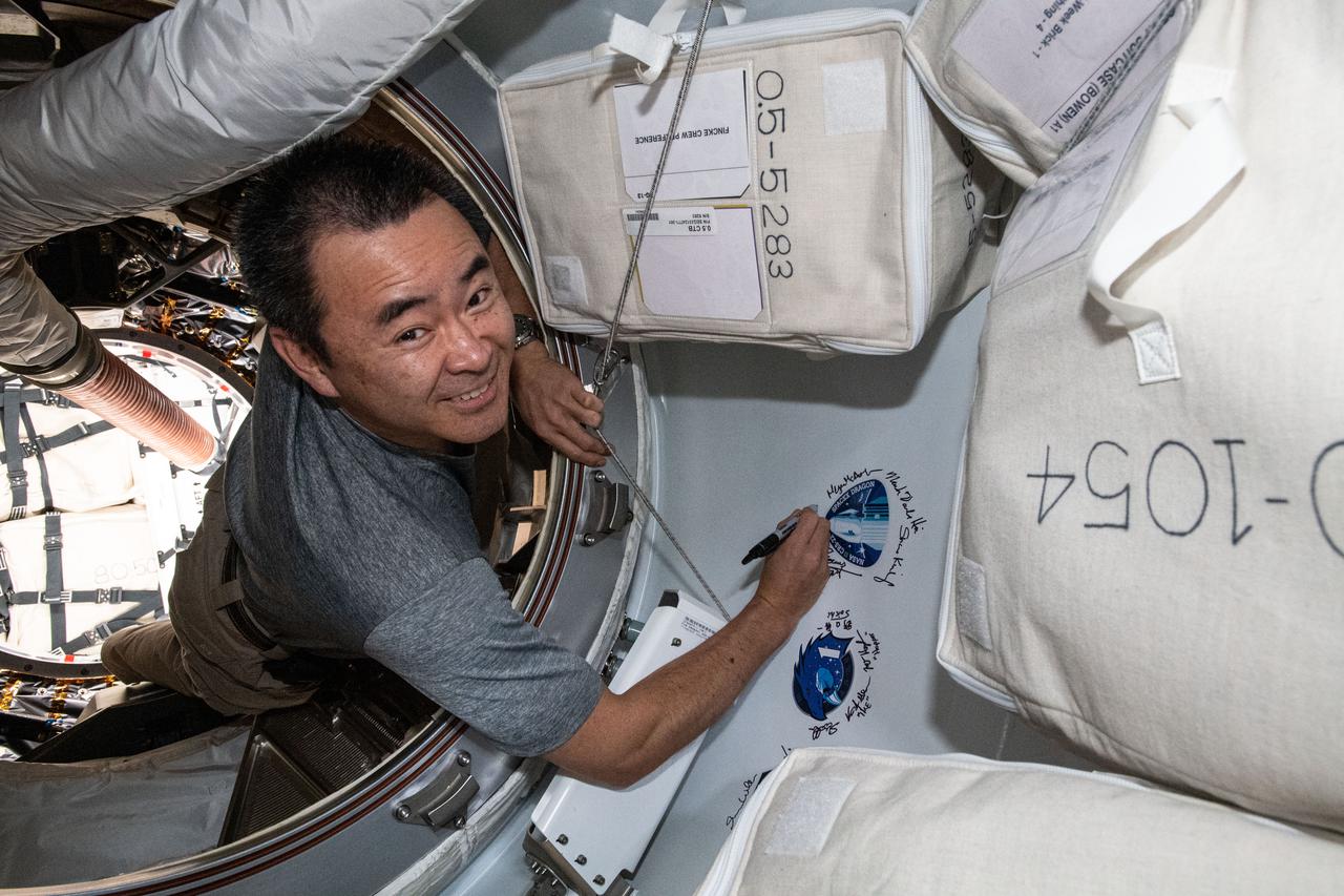 iss065e162509 (July 6, 2021) --- Expedition 65 Commander Akihiko Hoshide of the Japan Aerospace Exploration Agency (JAXA) signs his name next to the SpaceX CRS-22 cargo mission sticker attached to the vestibule between the SpaceX Cargo Dragon resupply ship and the Harmony module's space-facing international docking adapter.