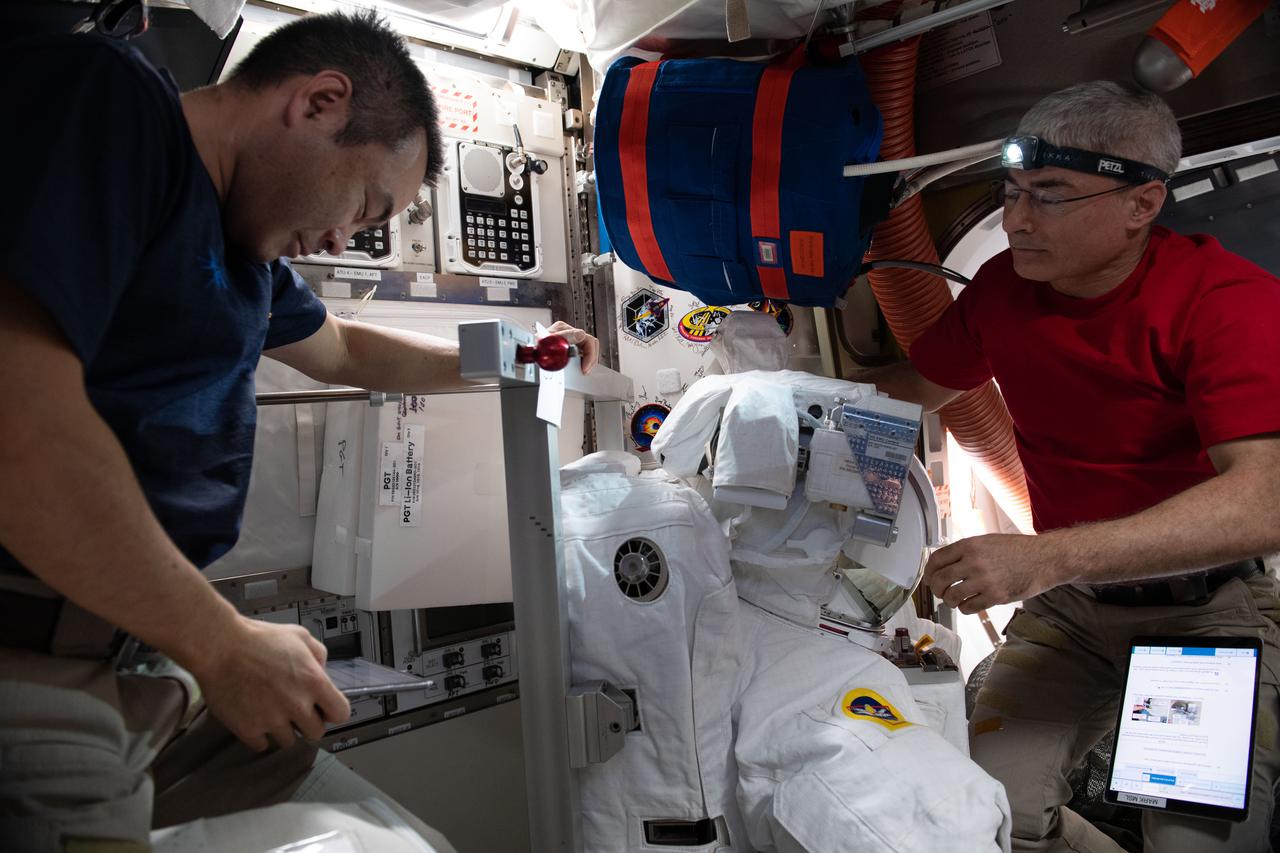 iss065e206754 (June 26, 2021) --- (From left) Expedition 65 Commander Akihiko Hoshide and Flight Engineer Mark Vande Hei install a high-definition camera assembly and lithium-ion power adapters on a U.S. spacesuit inside the International Space Station's Quest airlock.