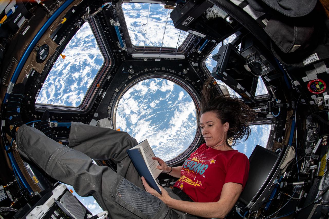 iss065e235640 (Aug. 11, 2021) --- NASA astronaut and Expedition 65 Flight Engineer Megan McArthur reads a book in the cupola, the International Space Station's "window to the world," while orbiting 265 miles above the northern Atlantic Ocean off the coast of Canada.