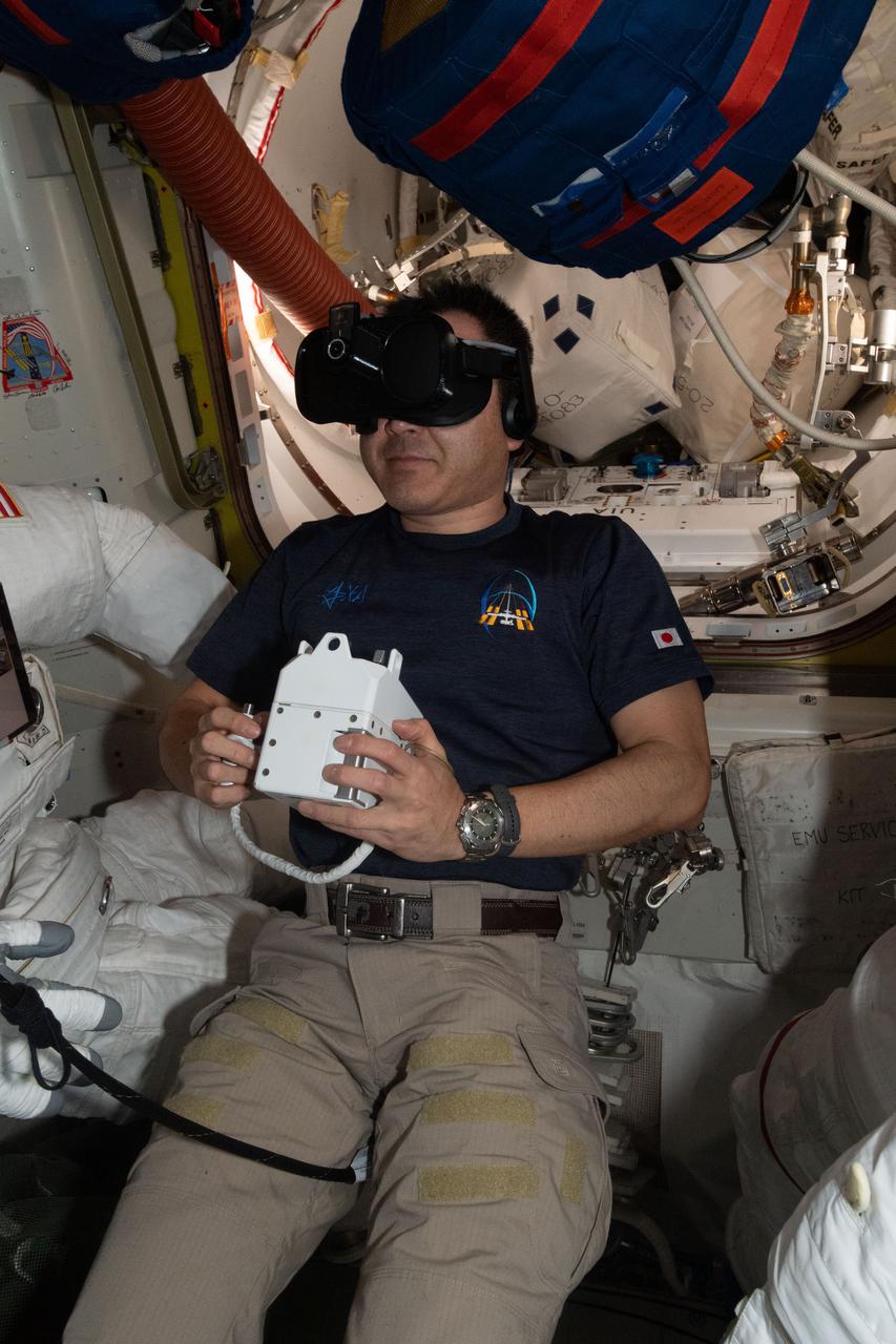iss065e238467 (Aug. 11, 2021) --- Expedition 65 Commander Akihiko Hoshide of the Japan Aerospace Exploration Agency (JAXA) wears virtual reality goggles inside the U.S. Quest airlock to train for an upcoming spacewalk at the International Space Station.
