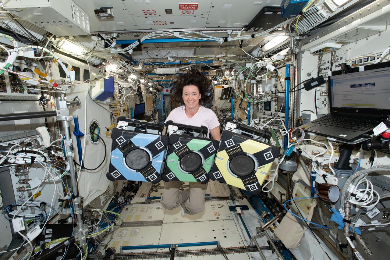 NASA astronaut Megan McArthur poses with the Astrobee robotic free-flyers in support of the Kibo Robot Programming Challenge (Robo-Pro Challenge). The Kibo-RPC, allows students to create programs to control Astrobee, a free-flying robot aboard the International Space Station (ISS).