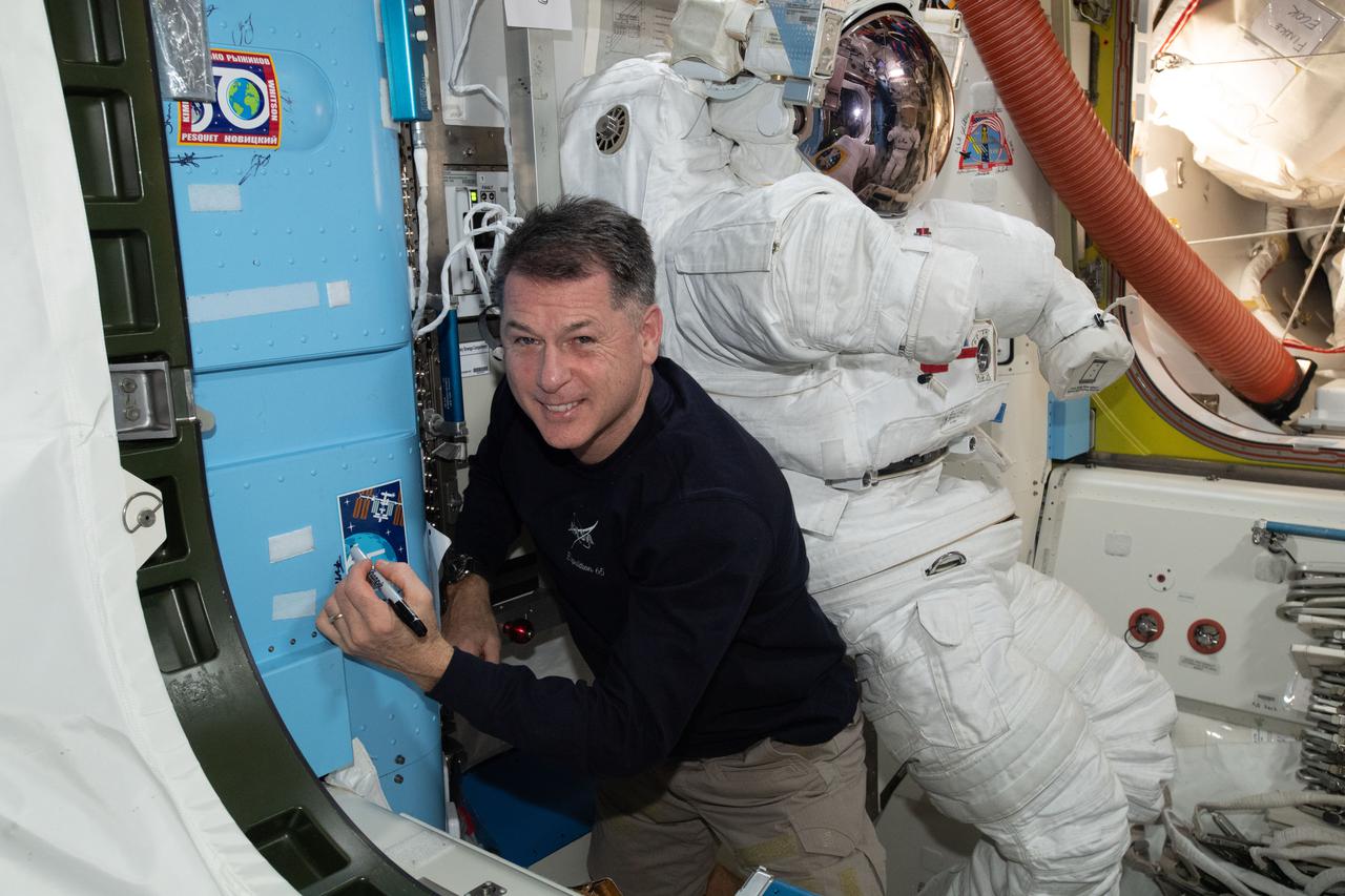 iss065e389550 (Sept. 17, 2021) --- NASA astronaut and Expedition 65 Flight Engineer Shane Kimbrough signs his name around the Expedition 65 mission insignia sticker affixed to the vestibule in between the Unity module and the Quest airlock.