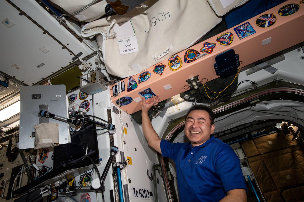 iss065e440612 (Oct. 4, 2021) --- Expedition 65 Flight Engineer Akihiko Hoshide of the Japan Aerospace Exploration Agency (JAXA) points to his mission's insignia sticker in the vestibule in between the International Space Station's Unity module and Tranquility module.