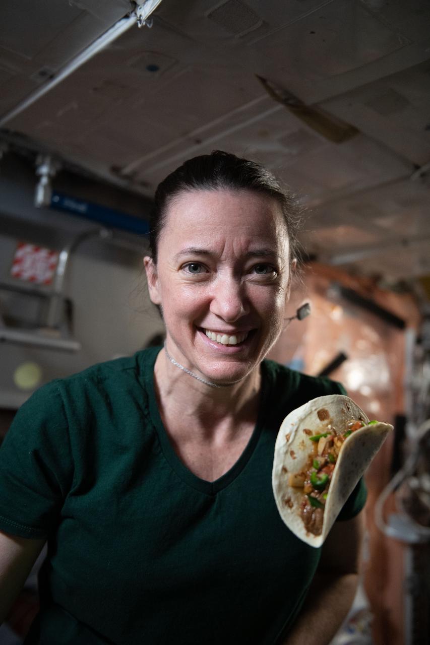 iss066e023198 (October 29, 2021) -- NASA astronaut and Expedition 66 flight engineer Megan McArthur is seen with a taco made using fajita beef, rehydrated tomatoes and artichokes, and chile peppers. The chile peppers were grown as part of the Plant Habitat-04 investigation aboard the International Space Station. The crop started growing on July 12, 2021, and represent one of the longest and most challenging plant experiments attempted aboard the orbiting laboratory. The chile peppers started growing on July 12, 2021, and represent one of the longest and most challenging plant experiments attempted aboard the orbiting laboratory. NASA astronaut and Expedition 66 flight engineer Mark Vande Hei conducted the first harvest of the pepper crop on October 29, 2021. Crew members sanitized the peppers and completed a scientific survey after their taste test. The Crew-3 astronauts will take over the crop when they arrive at the orbiting laboratory, and will conduct a final harvest of the peppers in late November. They will also sanitize and sample the crop, and complete surveys. Some peppers and their leaves from the final harvest will return to Earth for further analysis. What we learn will inform future crop growth and food supplementation activities for deep space exploration.