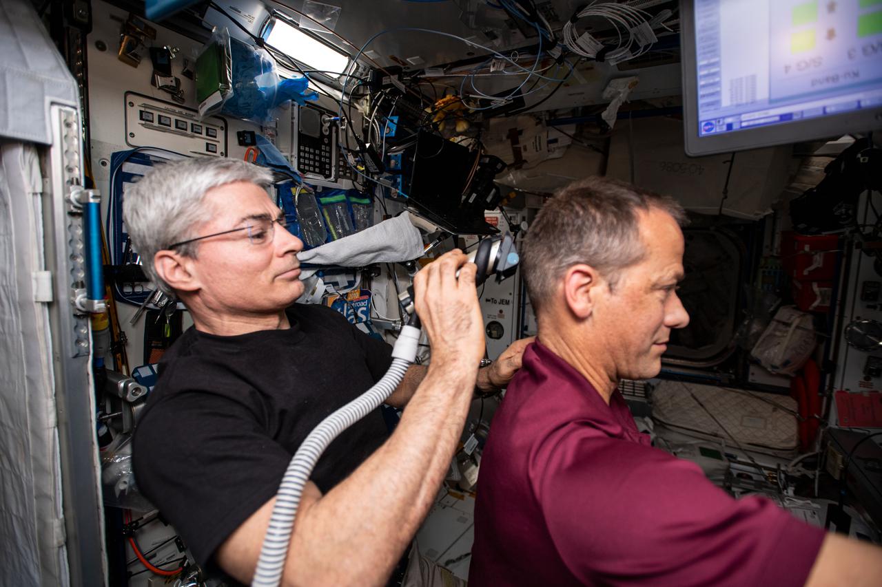 iss066e082911 (Nov. 25, 2021) --- The International Space Station is not just an orbital lab but also a home where astronauts can rest, pursue hobbies and even get a haircut. NASA astronaut and Expedition Flight Engineer Mark Vande Hei uses an electric razor with a vacuum attached that collects the hair he is cutting off of fellow NASA astronaut Thomas Marshburn.