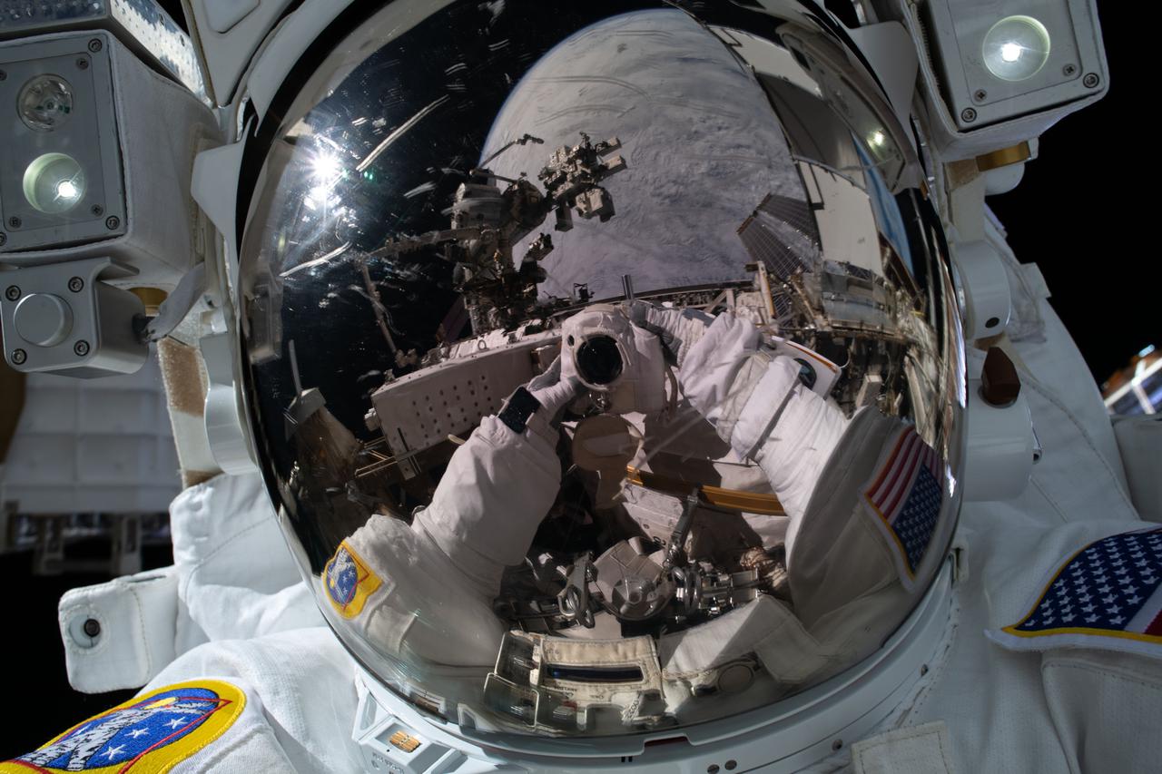 iss066e085978 (Dec. 2, 2021) --- NASA spacewalker Kayla Barron points the camera toward herself and takes an out-of-this-world "space-selfie" with her spacesuit's helmet visor down reflecting the International Space Station and the Earth more than 260 miles below.