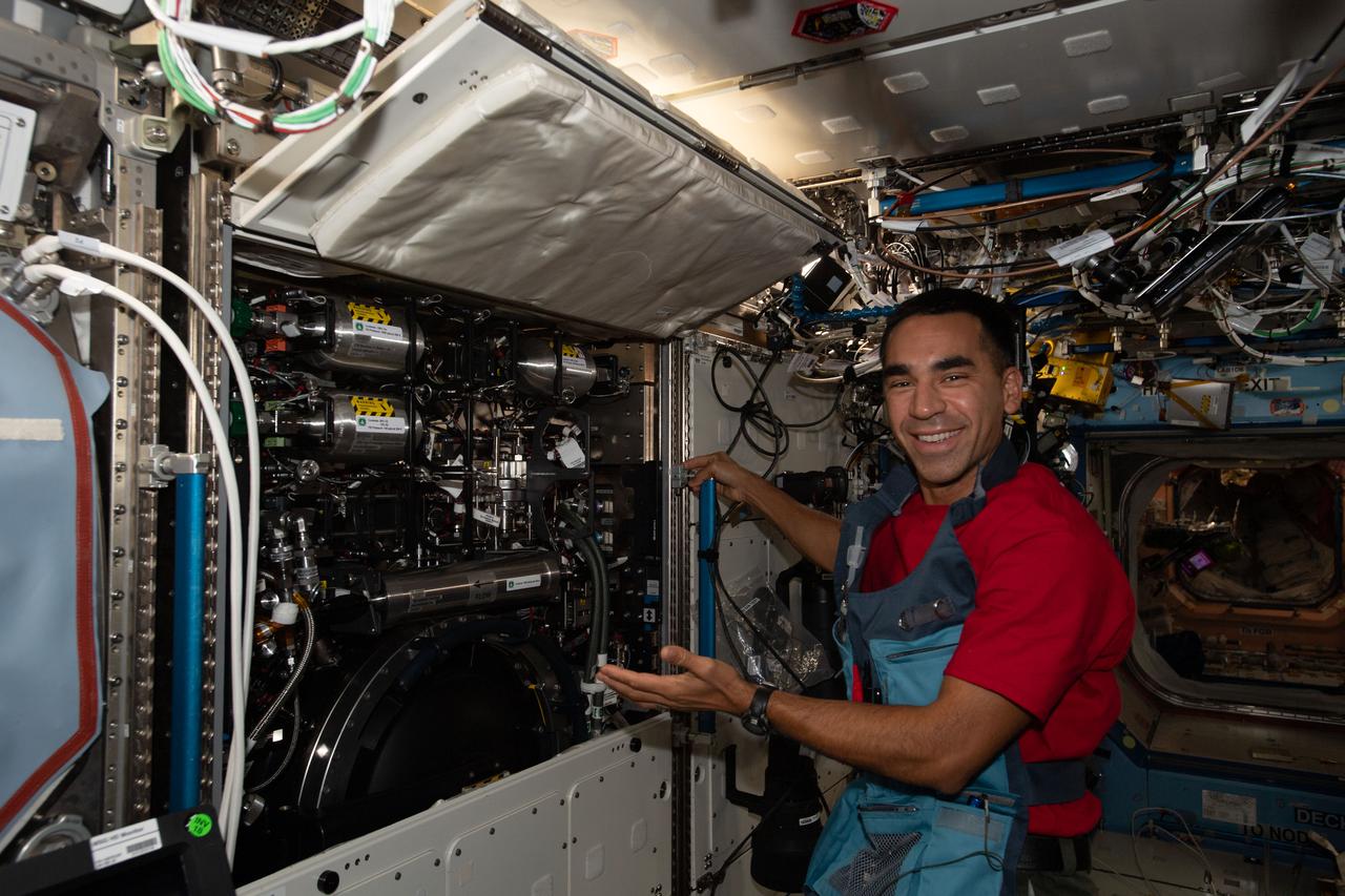 iss066e095422 (Dec. 21, 2021) --- NASA astronaut and Expedition 66 Flight Engineer Raja Chari displays the half-opened Combustion Integrated Rack aboard the International Space Station's U.S. Destiny laboratory module. The research device includes an optics bench, combustion chamber, fuel and oxidizer control, and five different cameras for performing combustion investigations safely in microgravity.