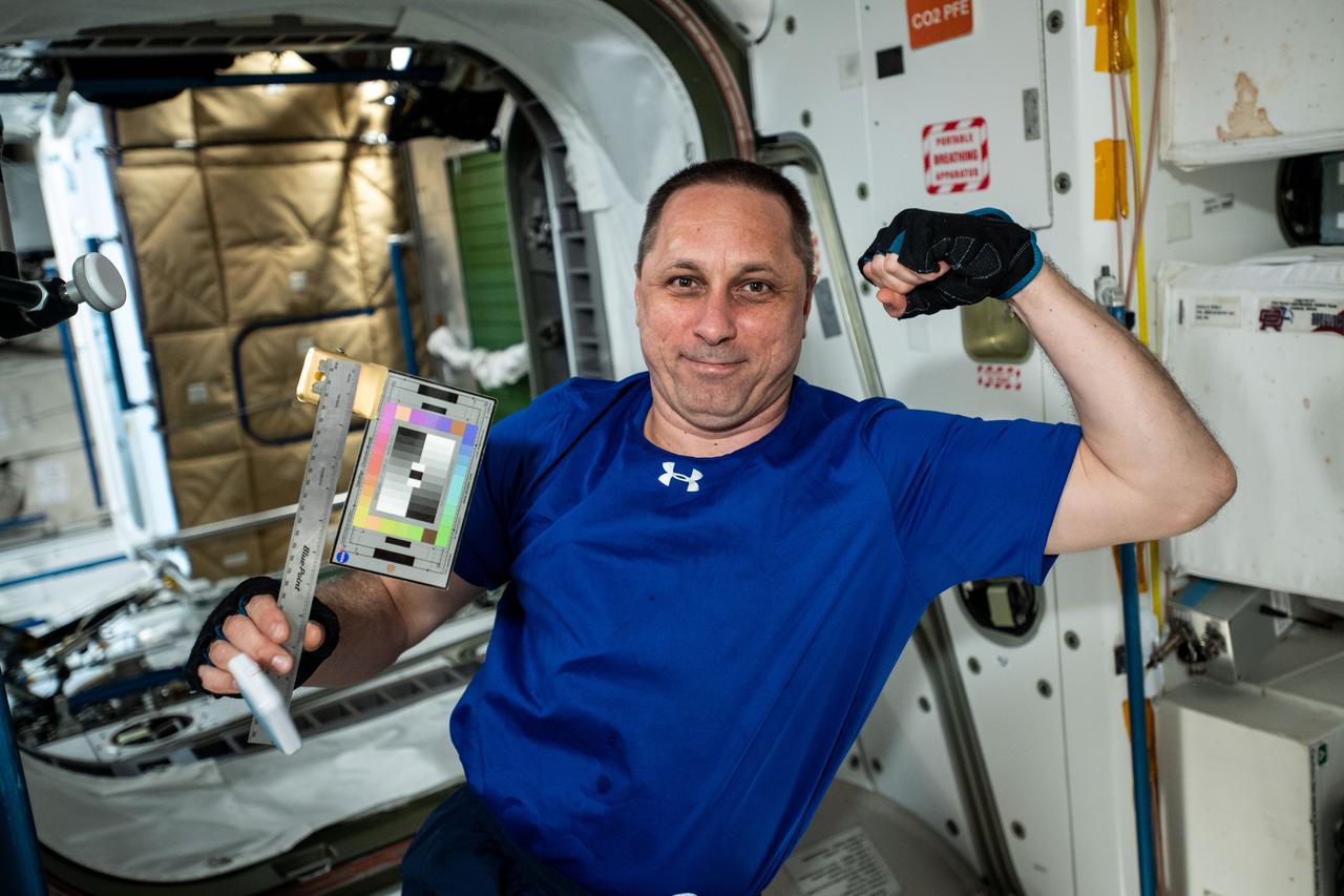 iss066e129776 (Jan. 28, 2022) --- Roscosmos cosmonaut and Expedition 66 Commander Anton Shkaplerov poses with a ruler and color chart aboard the International Space Station's Unity module. The ruler and chart are used for the SQuARES study looking at how crew members use different objects and spaces over time. This investigation may provide information that helps improve the design of future space craft and habitats.