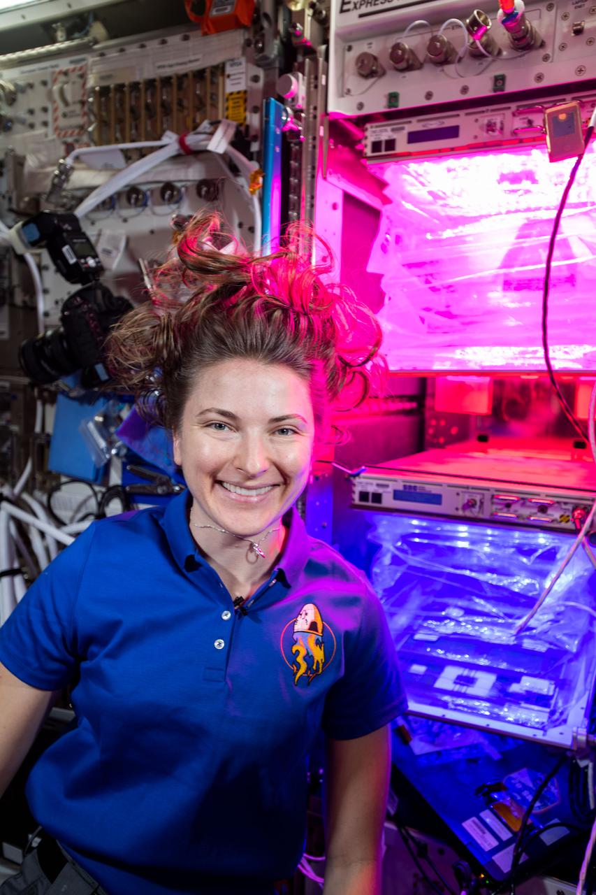 iss066e155817 (March 1, 2022) --- NASA astronaut and Expedition 66 Flight Engineer Kayla Barron poses for a portrait in front of the VEGGIE space botany facility inside the International Space Station's Columbus laboratory module.