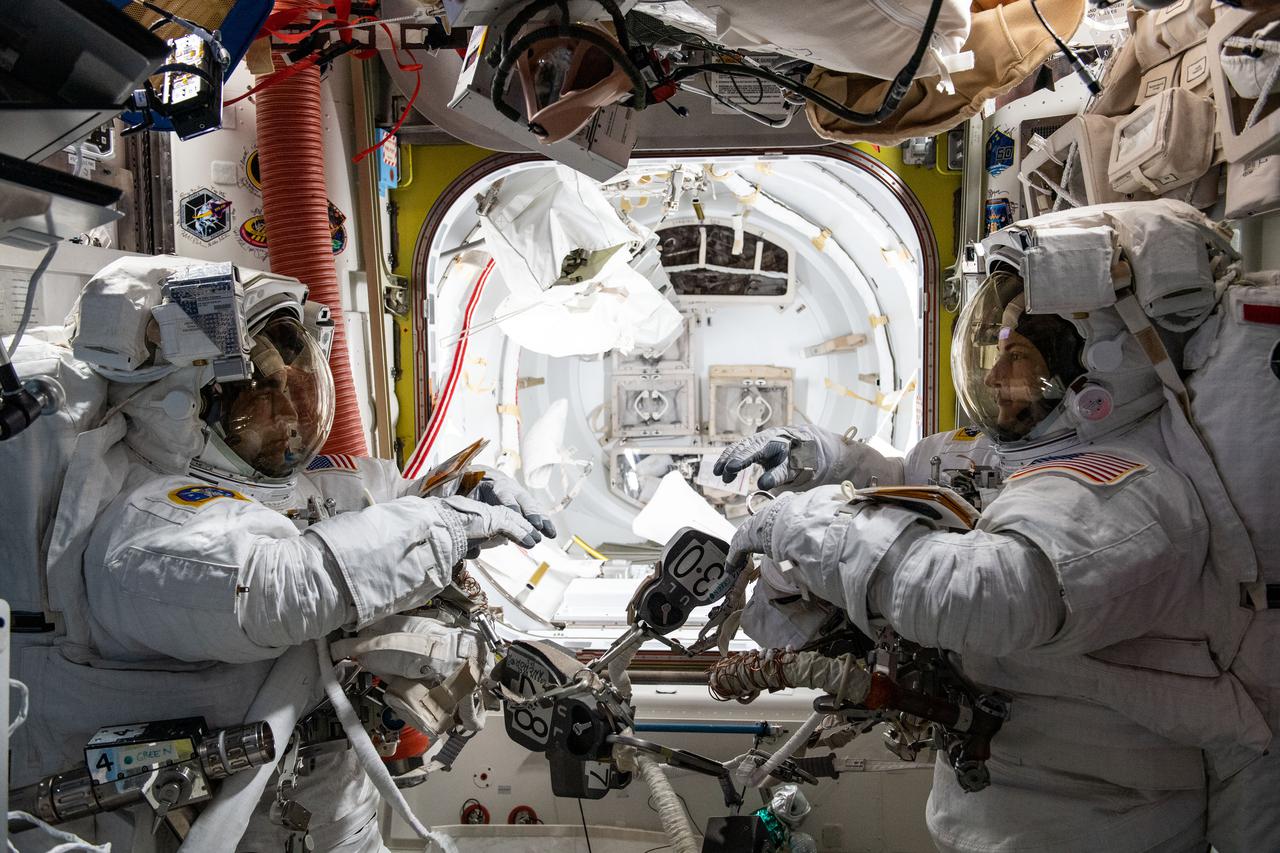 iss066e163039 (March 15, 2022) --- NASA astronauts (from left) Raja Chari and Kayla Barron are pictured inside the U.S. Quest airlock suited up and preparing for a six-hour and 54-minute spacewalk to set up the International Space Station for its next roll-out solar array.