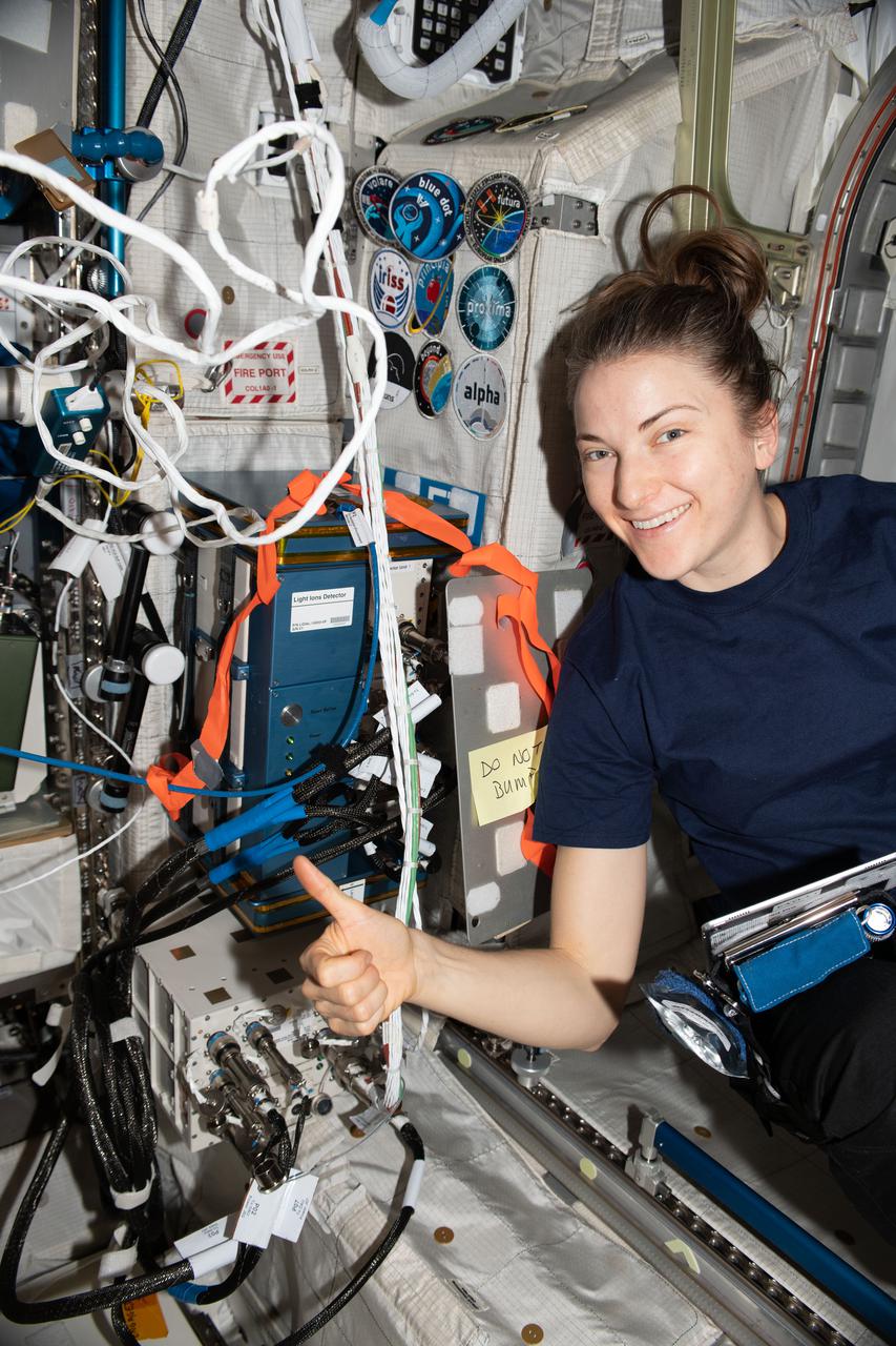 iss067e032549 (May 2, 2022) --- NASA astronaut and Expedition 67 Flight Engineer Kayla Barron begins her work day inside the International Space Station's Columbus laboratory module. She gives a "thumbs up" and poses next to the Light Ions Detector that monitors the radiation environment aboard the orbiting lab.