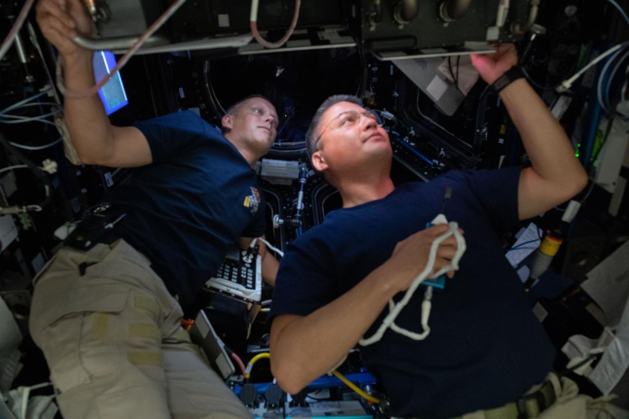 iss067e065667 (May 20, 2022) --- NASA astronauts (from left) Bob Hines and Kjell Lindgren are pictured inside the International Space Station's seven-windowed cupola monitoring the approach and rendezvous of Boeing's CST-100 Starliner spacecraft on the company's Orbital Flight Test-2 mission.