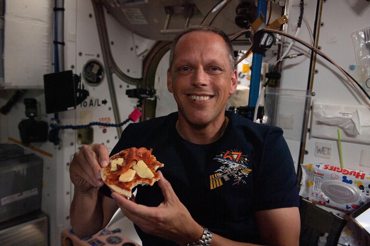 iss067e089041 (May 27, 2022) --- NASA astronaut and Expedition 67 Flight Engineer Bob Hines enjoys a personal size pizza during dinner time aboard the International Space Station.