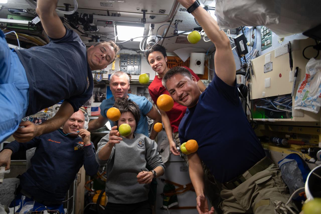 iss067e117737 (June 3, 2022) --- Expedition 67 crew members pose with fresh fruit flying weightlessly in microgravity delivered recently aboard the Progress 81 (81P) cargo craft. The 81P docked to the Zvezda service module's rear port aboard the International Space Station after a three-and-half-hour trip that began with a launch from the Baikonur Cosmodrome in Kazakhstan. Pictured clockwise from left are, Roscosmos Flight Engineers Sergey Korsakov and Denis Matveev; NASA Flight Engineers Jessica Watkins and Kjell Lindgren; ESA (European Space Agency) Flight Engineer Samantha Cristofretti; and Roscosmos Commander Oleg Artemyev.
