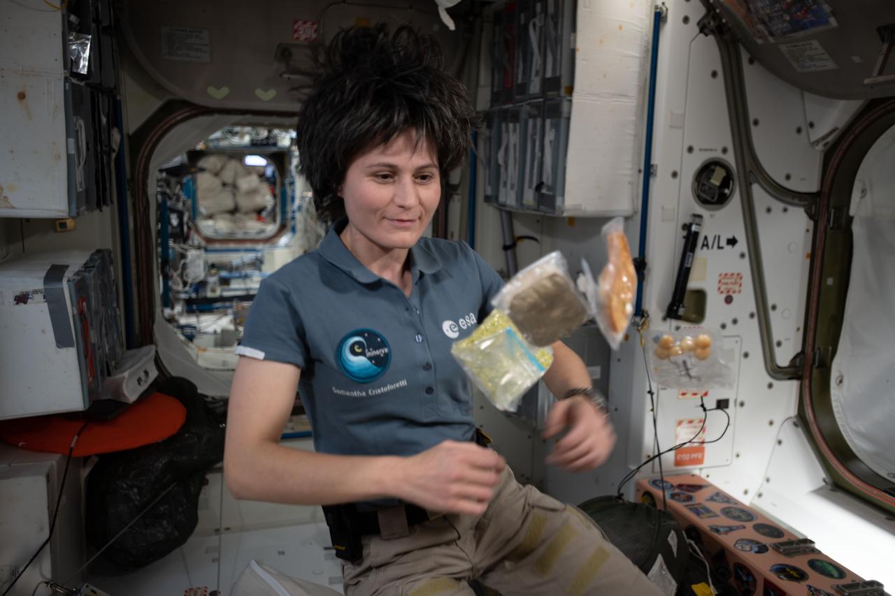 iss067e170528 (July 2, 2022) --- Expedition 67 Flight Engineer and ESA astronaut (European Space Agency) Samantha Cristoforetti poses with food packets flying weightlessly inside the International Space Station's Unity module.