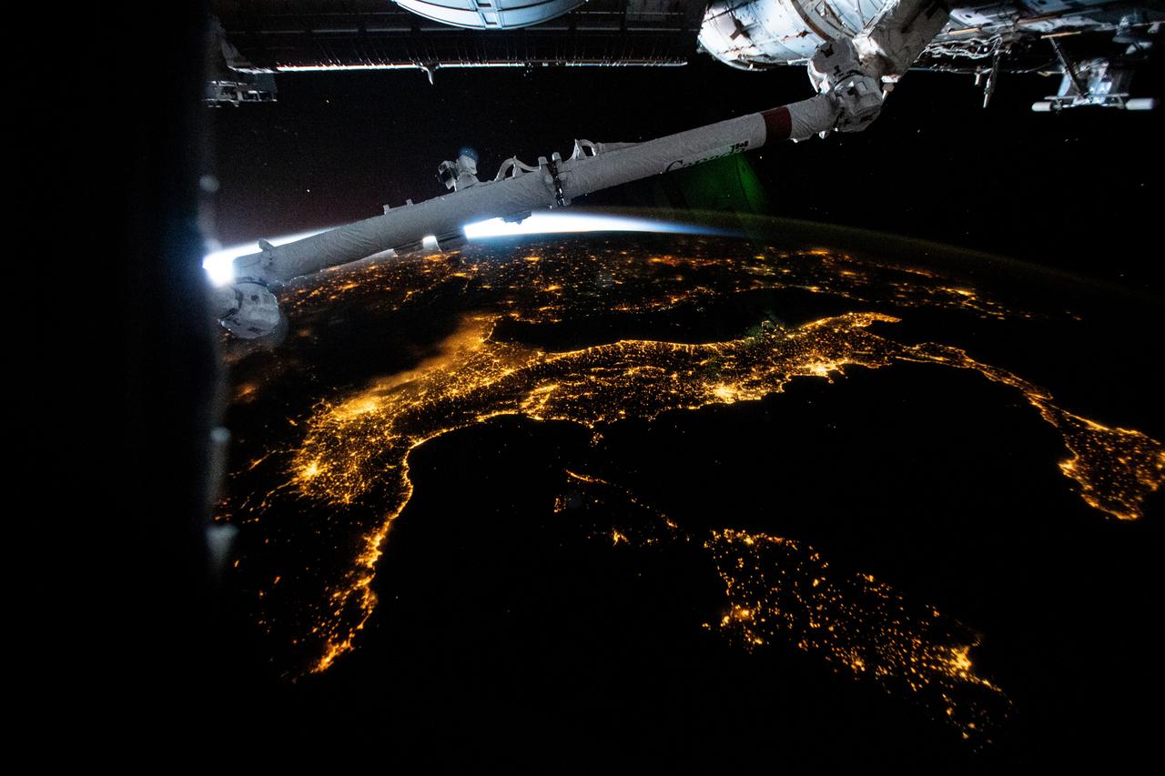iss067e176401 (July 4, 2022) --- The city lights of Italy, including the French island of Corse and Italian islands of Sardinia and Sicily, are pictured from the International Space Station from 261 miles above the Mediterranean Sea while flying into an orbital sunrise. In the top foreground, is a portion of the Candarm2 robotic arm.