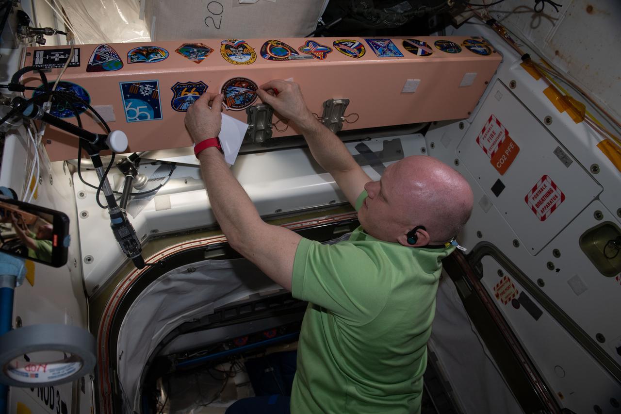 iss067e378813 (Sept. 21, 2022) --- Expedition 67 Commander Oleg Artemyev affixes his mission's insignia sticker to the inside of the International Space Station's Unity module. Artemyev, along with Roscosmos Flight Engineers Denis Matveev and Sergey Korsakov, would depart the orbiting lab on Sept. 29 inside the Soyuz MS-21 crew ship for a parachute-assisted landing in Kazakhstan ending a six-month space research mission.