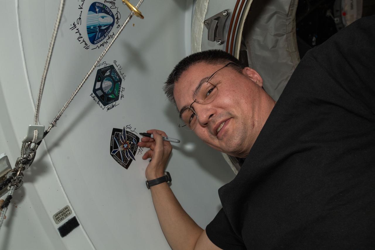 iss068e016454 (Oct. 12, 2022) --- NASA astronaut and Expedition 68 Flight Engineer Kjell Lindgren, also the SpaceX Crew-4 Commander, signs his name around the Crew-4 mission insignia affixed to the vestibule between the Harmony module's space-facing port and the Dragon Freedom crew ship.