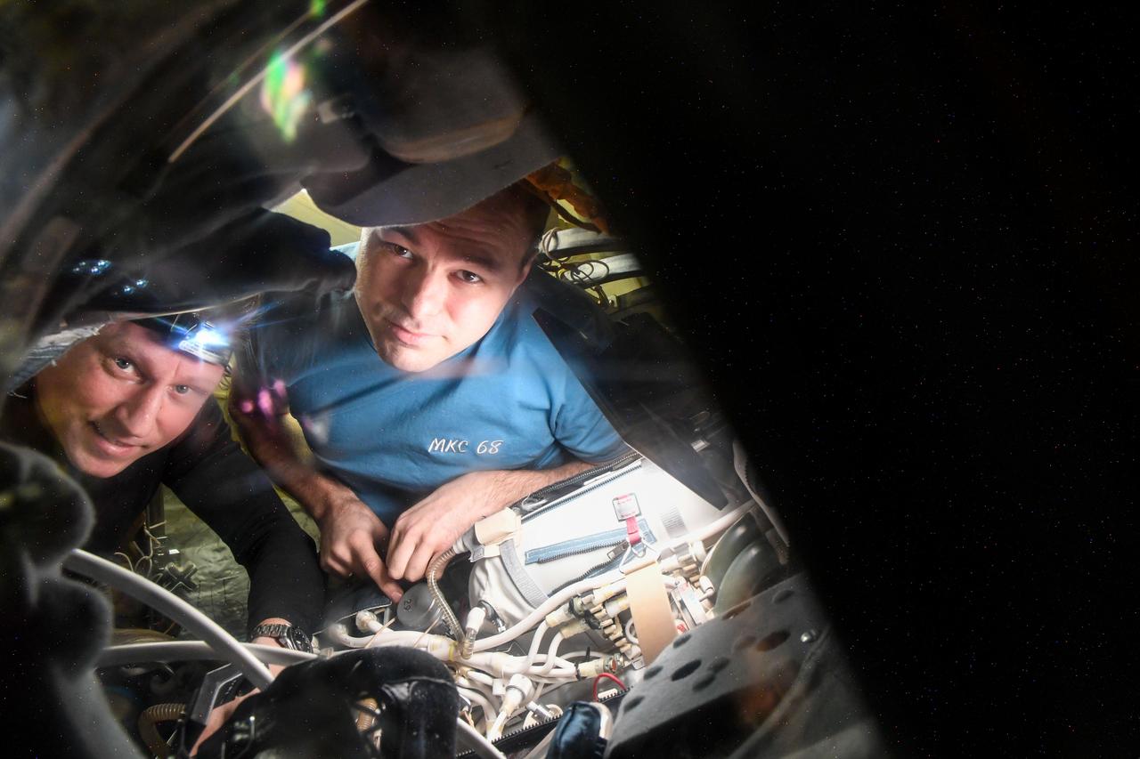 iss068e027429 (Dec. 5, 2022) --- Roscosmos cosmonauts (from left) Sergey Prokopyev and Dmitri Petelin service components inside an Orlan spacesuit aboard the International Space Station's Poisk module. Credit: Roscosmos